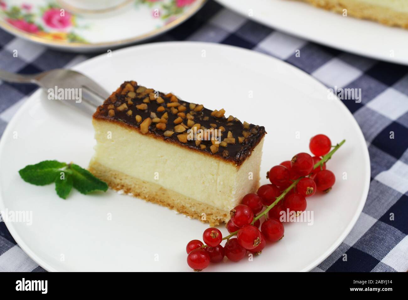 Slice of baked cheesecake with chocolate topping sprinkled with nuts and red current Stock Photo