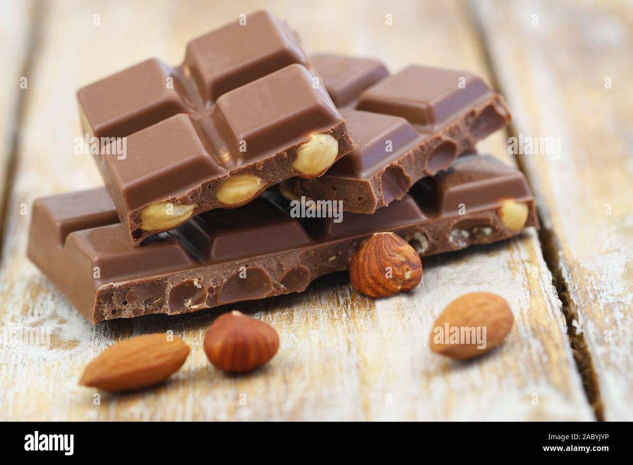 Milk chocolate pieces with whole hazelnuts and almonds on rustic wooden surface Stock Photo
