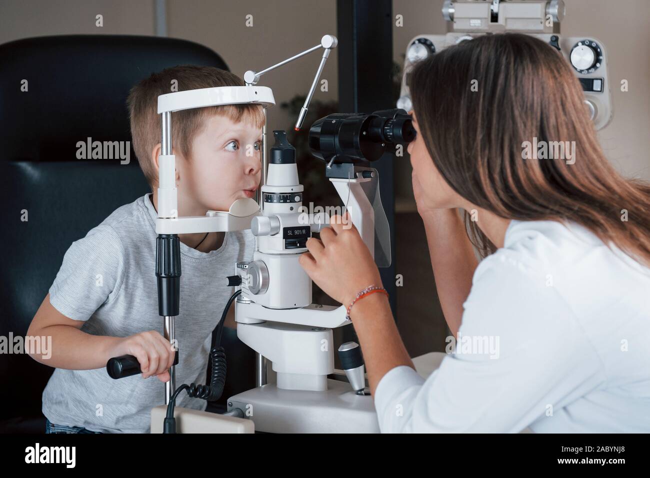 Making funny faces. Little boy having test for his eyes with special optical apparatus by female doctor Stock Photo