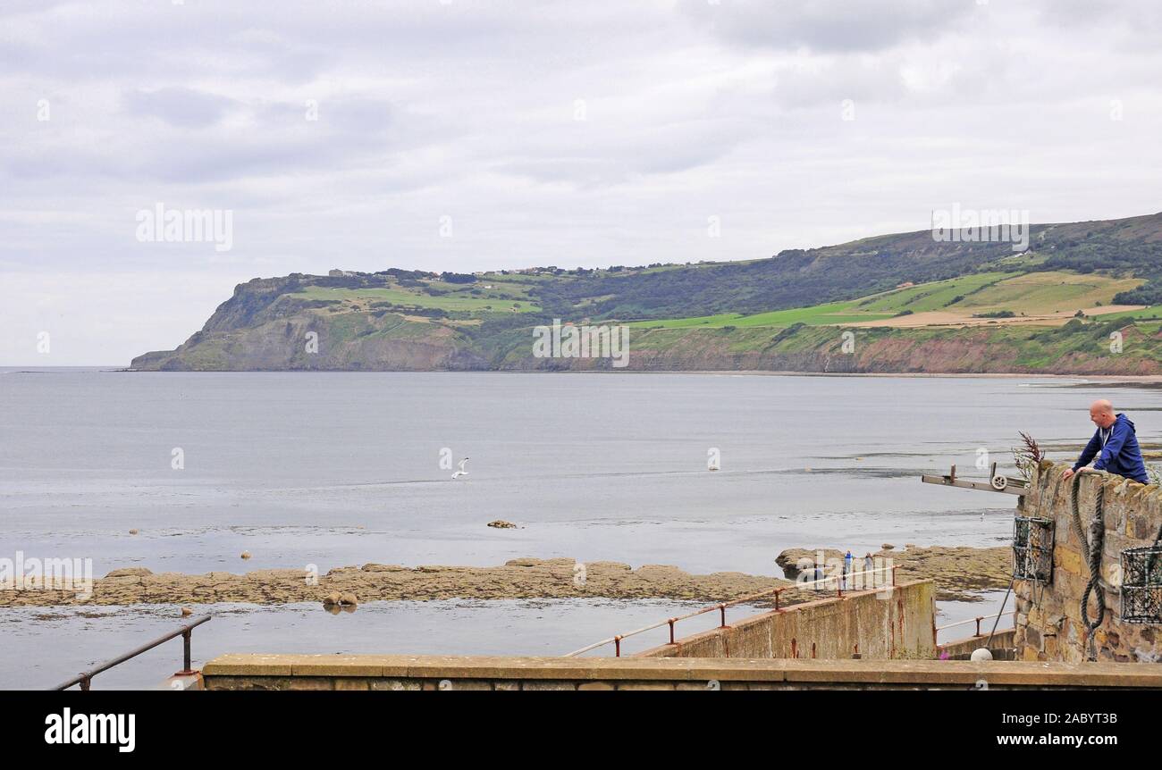 Man looking down at the beach.  Receding tide.  Robin Hood's Bay.  From the sea wall. Stock Photo