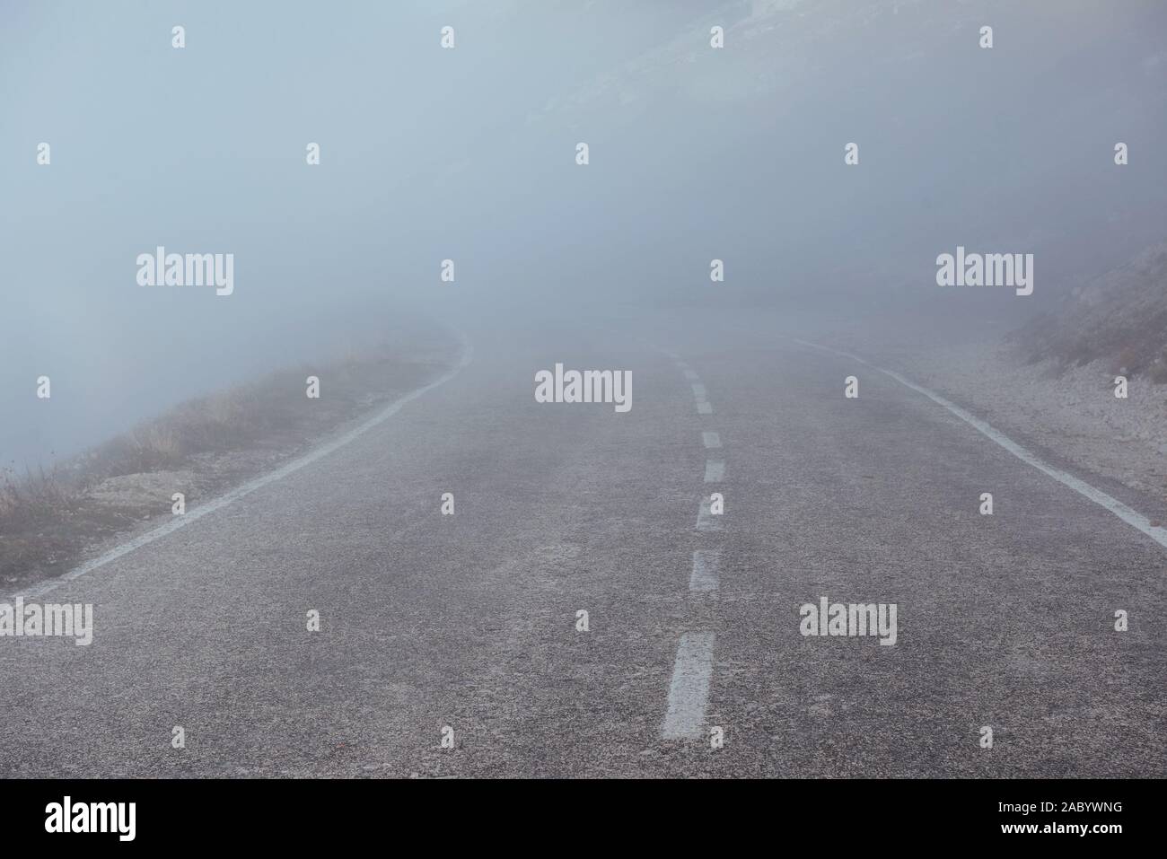 Mysterious looking road in the heavy fog near the mountains Stock Photo
