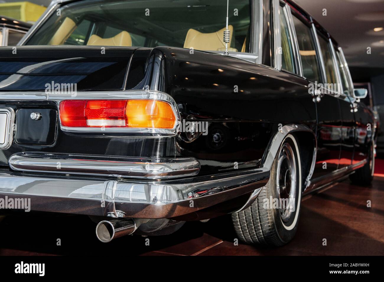 Back and side view of black retro business class limousine with right backlight, chrome mirror and wheel arch, whitewall tire on brown floor Stock Photo