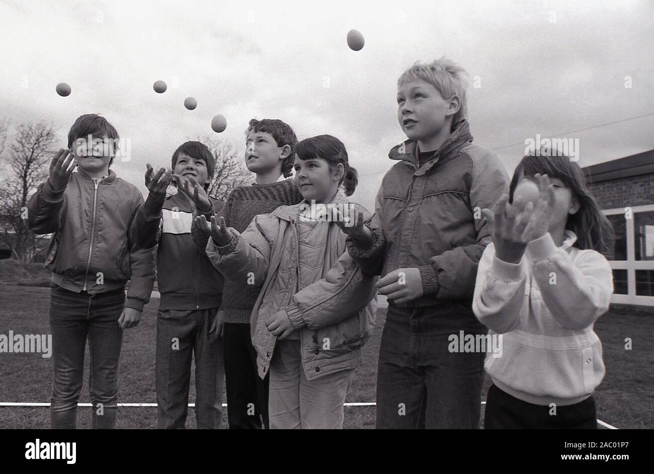 1980s, historical, children practising throwing and catching an egg i preparation for the traditional egg throwing competition, England, UK.  Egg throwing is a two person activity requiring distance lobbing and the ability to catch. Each team member begins by standing ten metres apart, spreading out after each successful catch. But....drop or break the egg and you are out!  It is believed that egg throwing first occurred in the 1300s, gradually becoming an informal sport called the 'egg toss', played at country fairs and fetes. Stock Photo