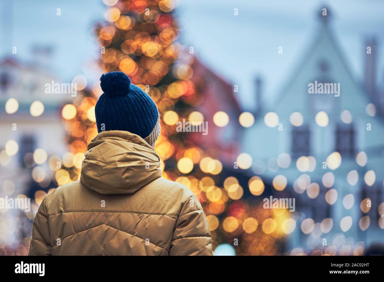 Rear view of man in warm clothing during walk in city. Christmas tree and decoration in Old Town in Tallinn, Estonia. Stock Photo