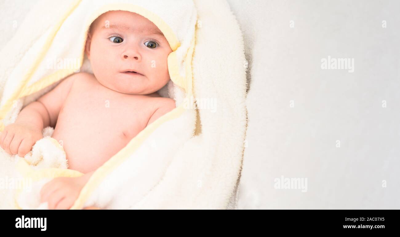 Adorable 6 months old Baby girl infant on a bed on her belly with head up looking into camera with her big eyes. Natural light. Stock Photo