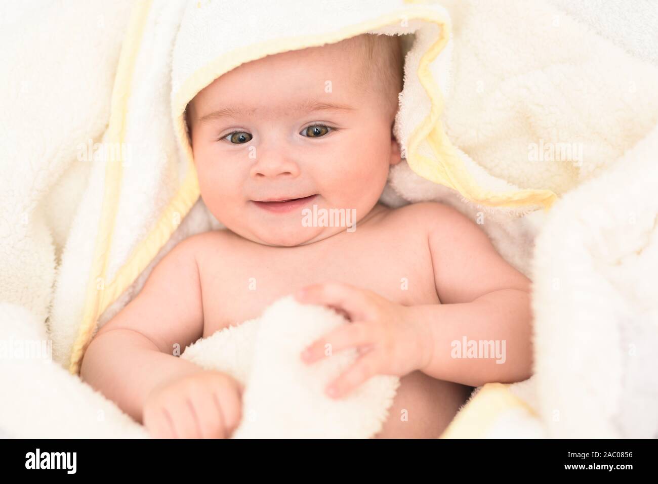 Adorable 6 months old Baby girl infant on a bed on her belly with head up looking into camera with her big eyes. Natural light. Stock Photo