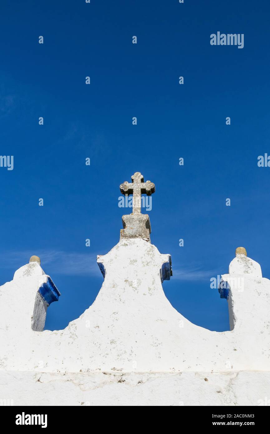 Close up top part of a classic white painted Portuguese parish church showing white painted wall and cross against a clear blue sky Stock Photo