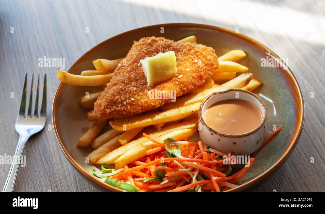 fried fish filet with french fries and veggies on plate in restaurant Stock Photo