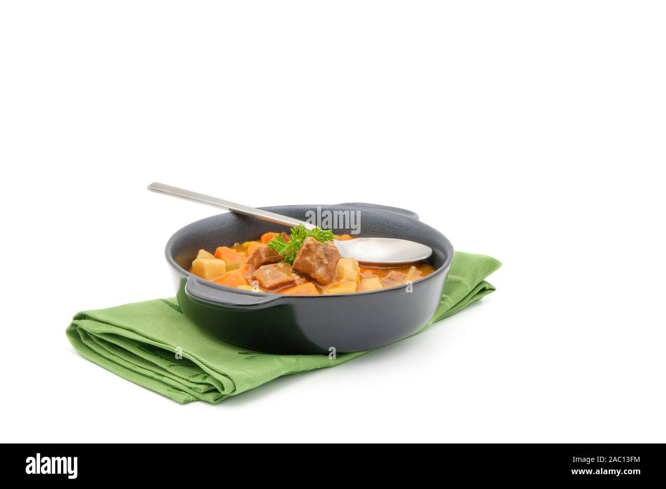 Bowl of hearty beef stew on a green napkin on a white background. Stock Photo