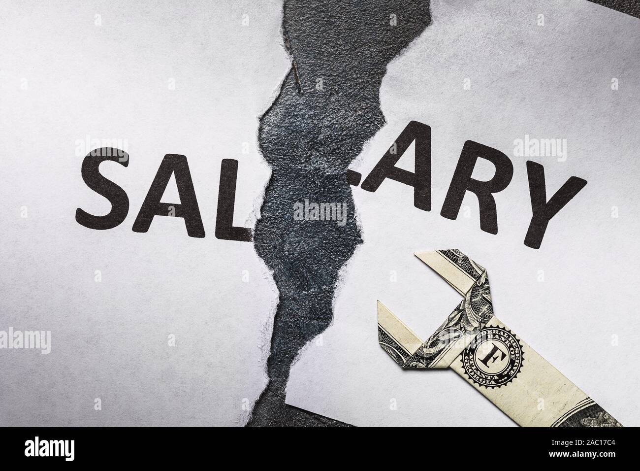 A sheet of white paper with the words salary, torn in half. Low wages require regulation Stock Photo