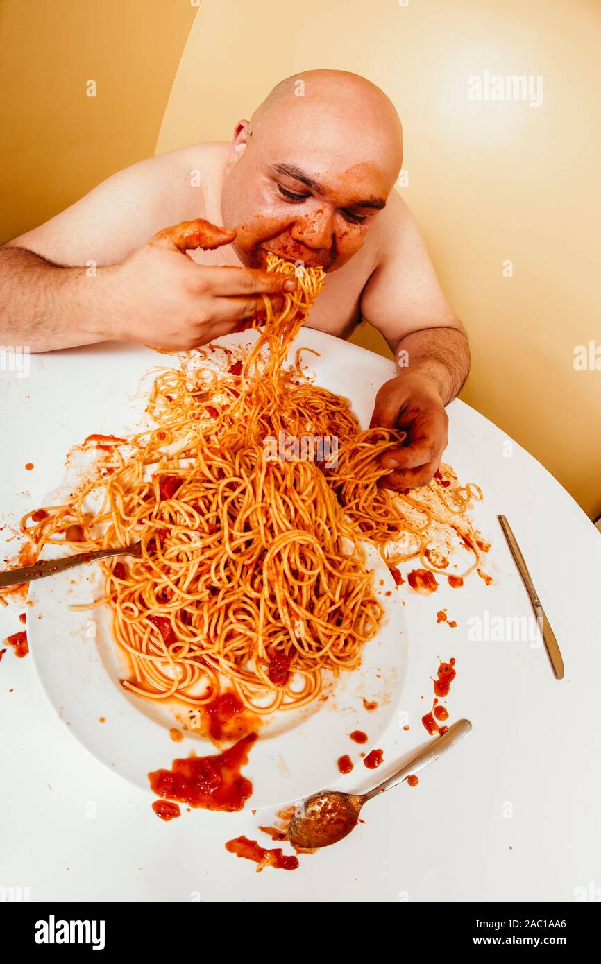 Photo of an overweight bald man enjoying a plate of spaghetti. Shot with fish-eye lens. Stock Photo