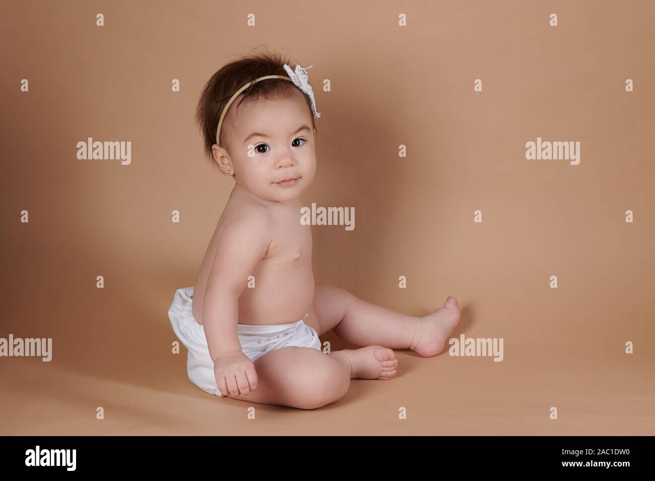 One baby girl sitting on brown color studio background Stock Photo