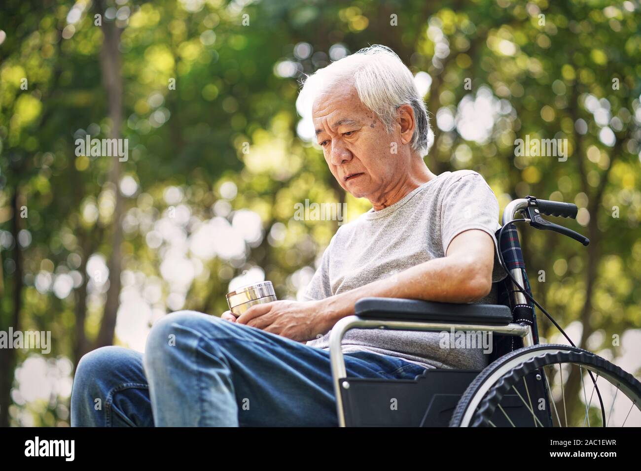 asian old man sitting in a wheelchair with head down looking sad and depressed Stock Photo