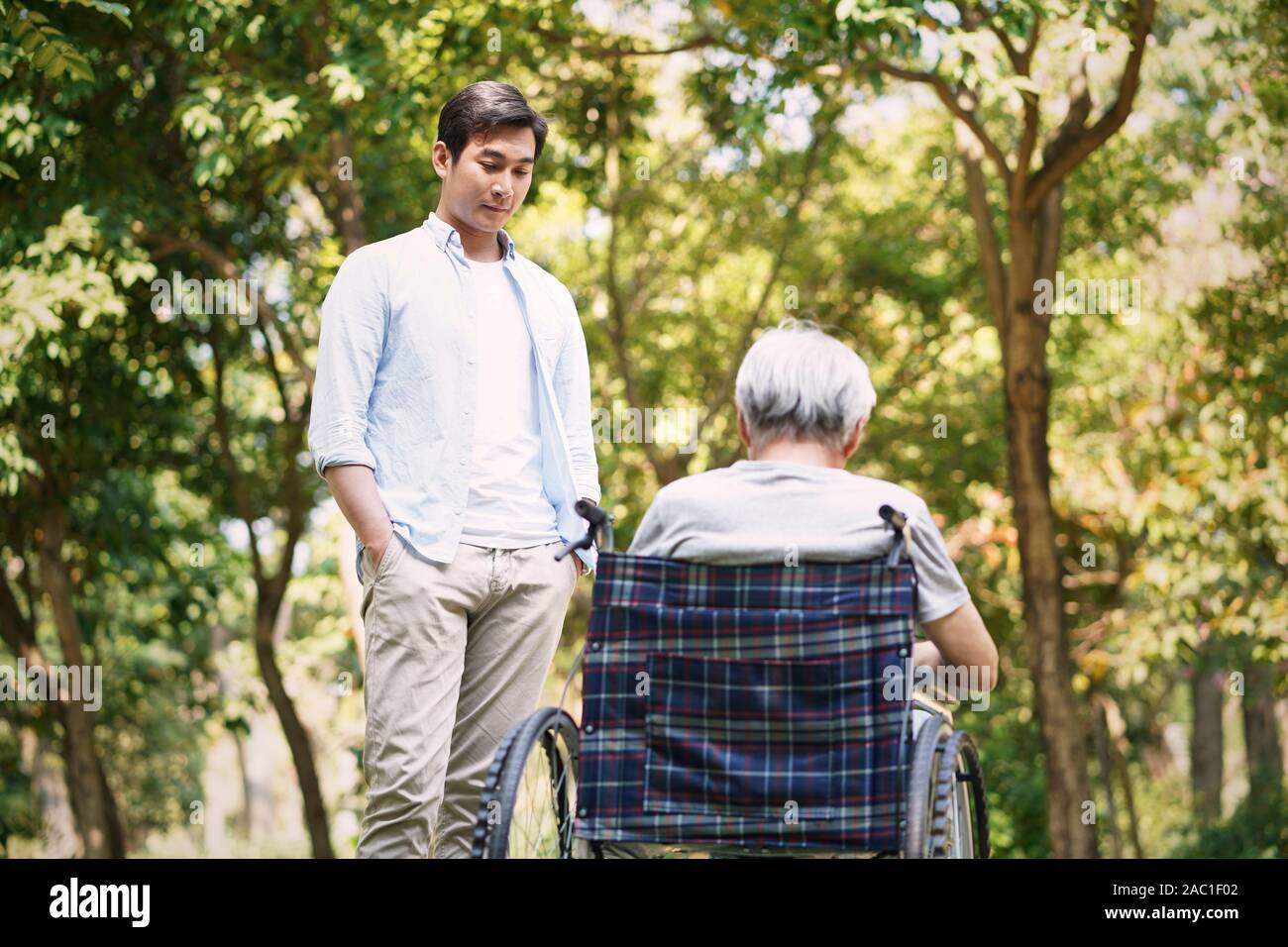 asian son talking to sad and depressed wheelchair bound father Stock Photo