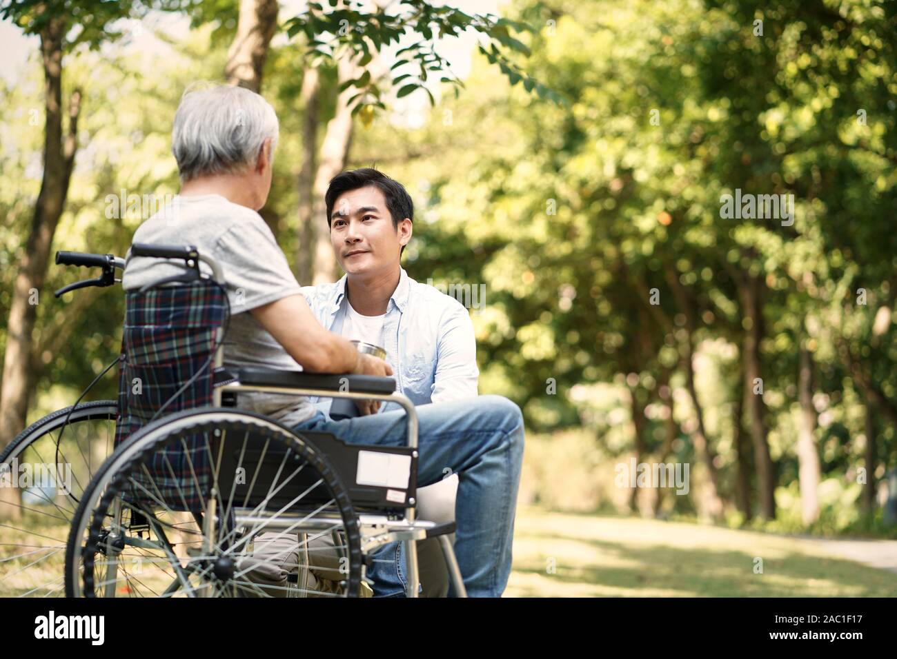 asian son talking to and comforting wheelchair bound father Stock Photo