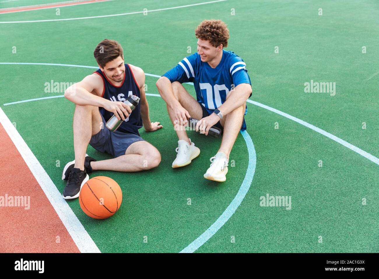 Two attarctive fit men basketball players sitting on a sports ground, talking Stock Photo