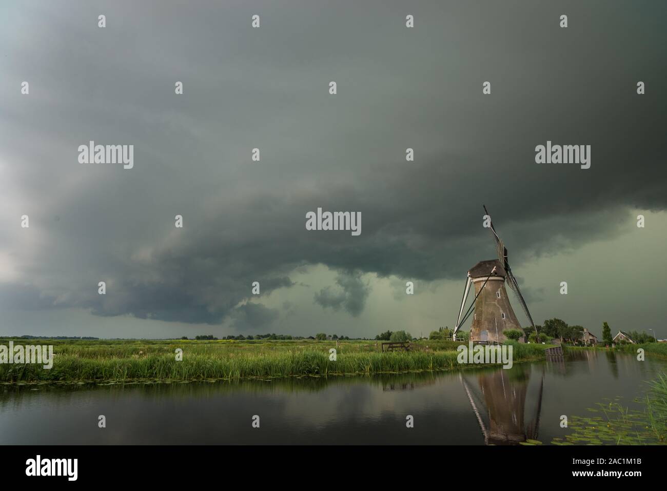 Calm before the storm. Windmill and dramatic green sky below a shelfcloud of a severe thunderstorm in The Netherlands. Stock Photo