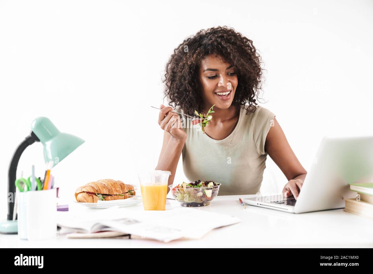 Beautiful smiling young african woman sitting at the desk isolated over ...