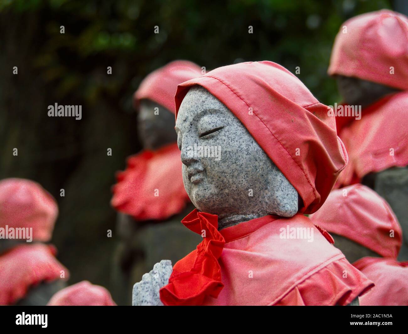 Jizo stone statues wearing a red apron in a shrine garden, Tokyo, Japan