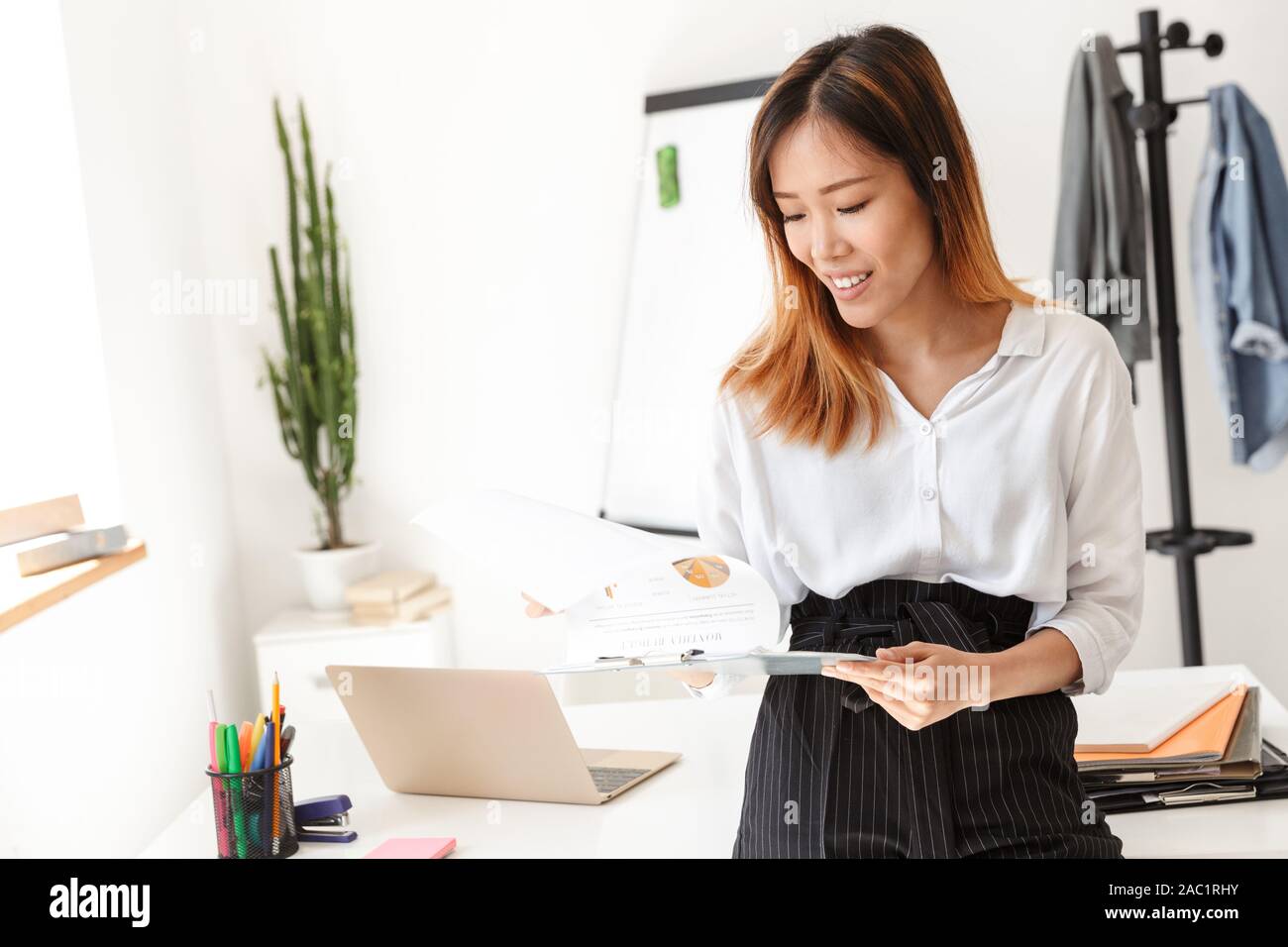 Beautiful smiling young asian businesswoman standing at her desk in ...