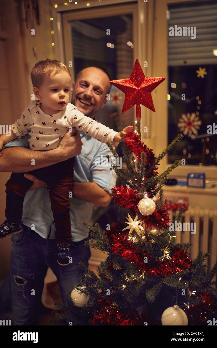 Baby and smiling father decorate the Christmas tree together Stock Photo