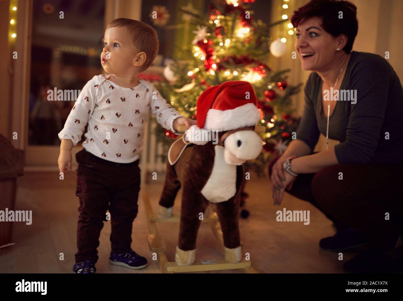 Suprised baby and his toy horse by the decorated Christmas tree Stock Photo