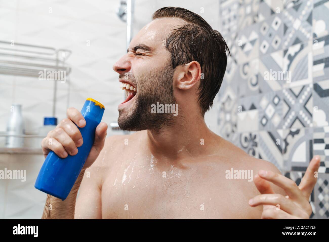Attractive young cheerful man singing while washing in the shower