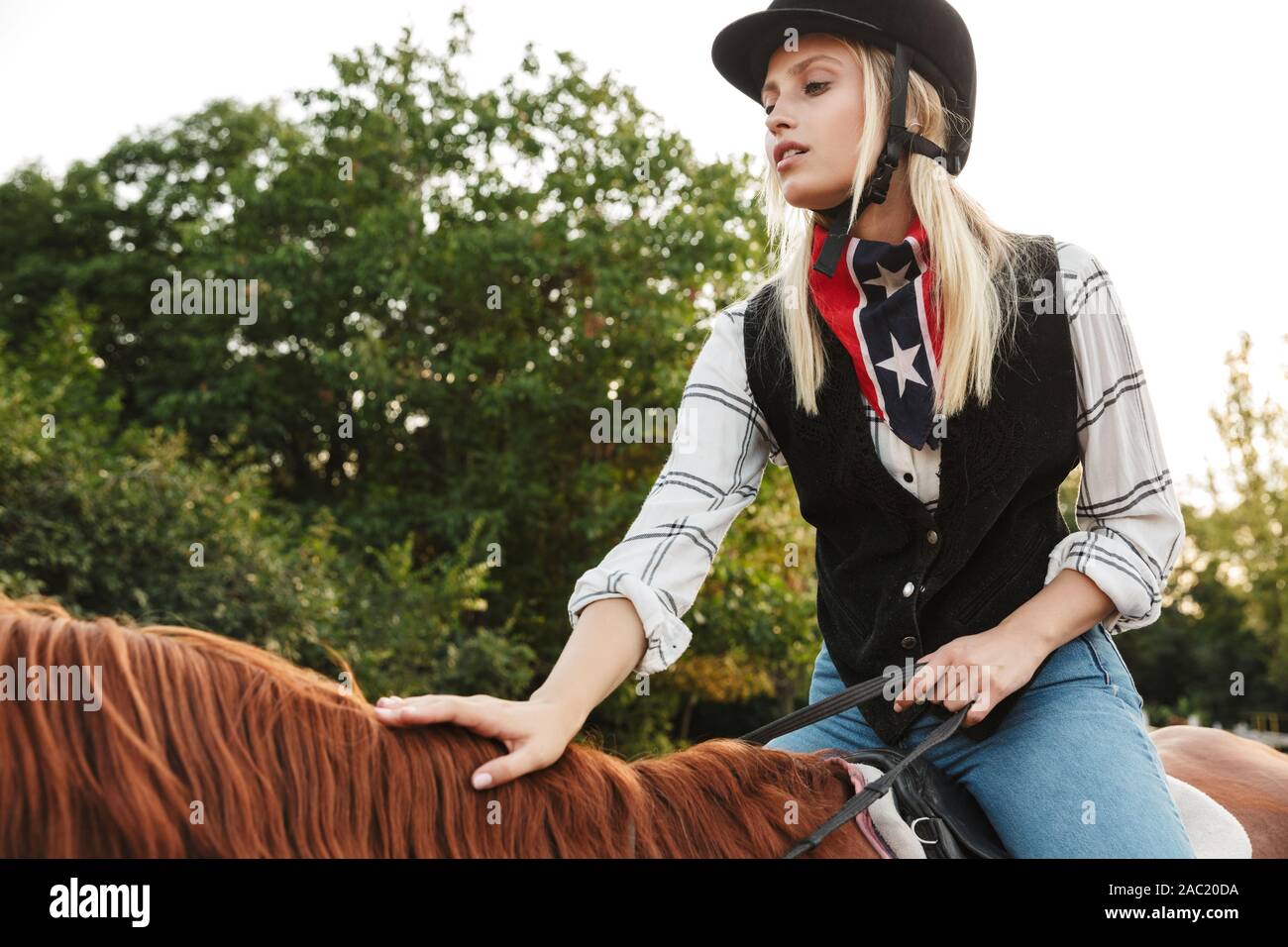 Image of caucasian young blonde woman wearing hat riding horse at yard