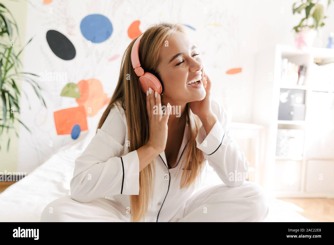 Photo of emotional young cute girl in pajama at home on bed listening