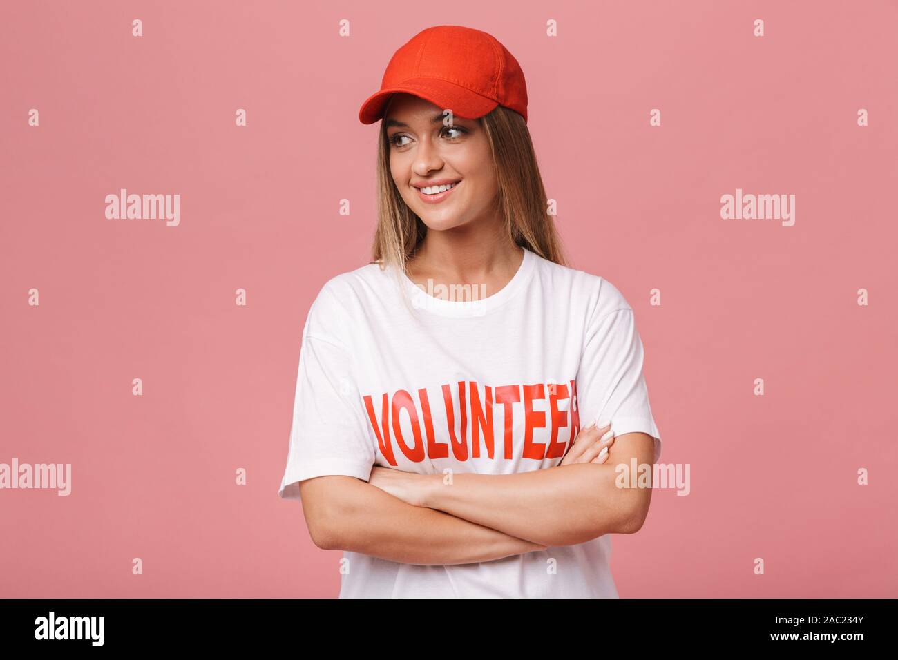 Happy confident young volunteer girl standing isolated over pink background, arms folded Stock Photo