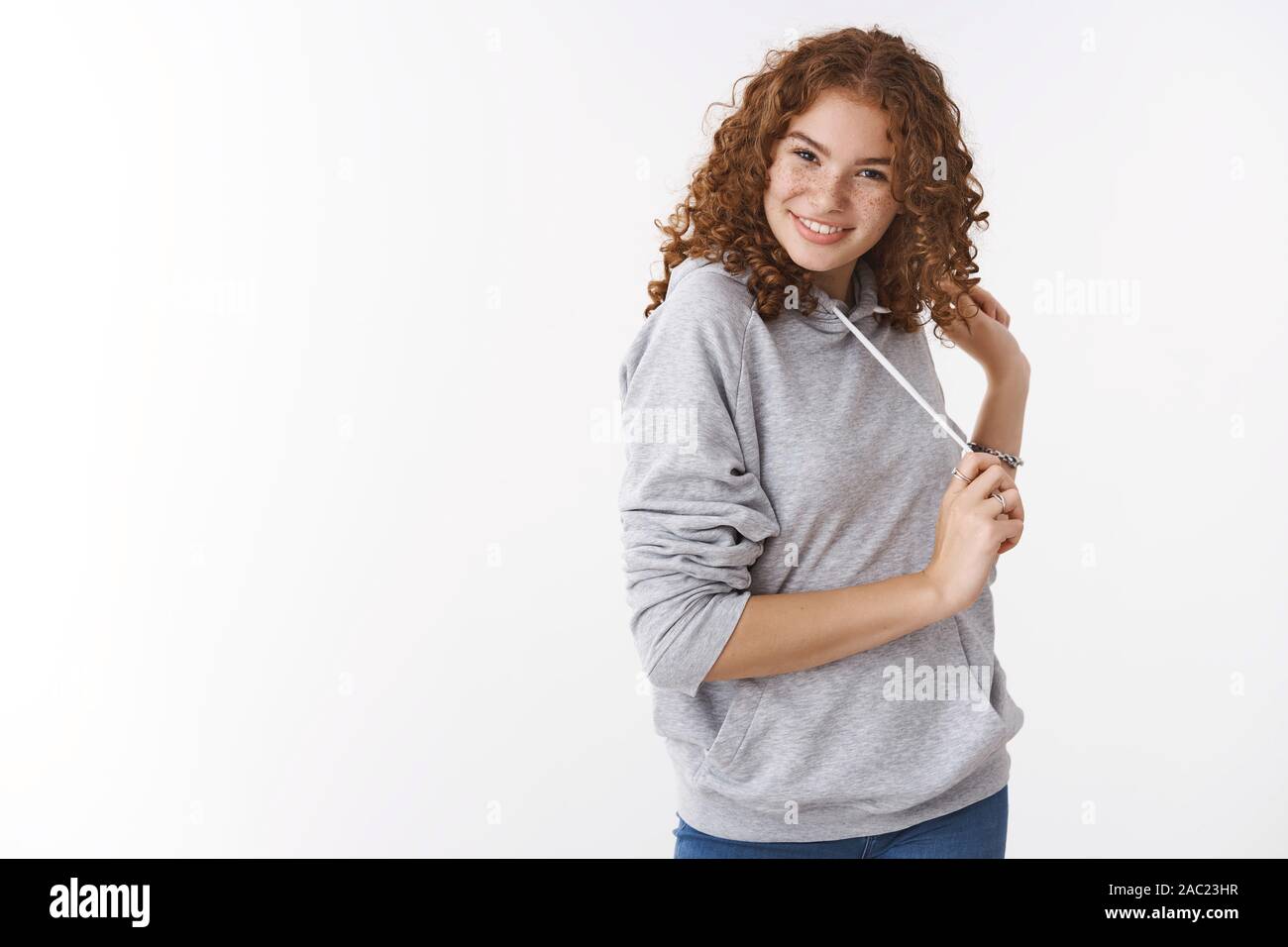 Studio shot cheeky cheerful redhead charismatic young girl wearing grey hoodie smiling silly flirting giggling playing hair wearing grey casual hoodie Stock Photo