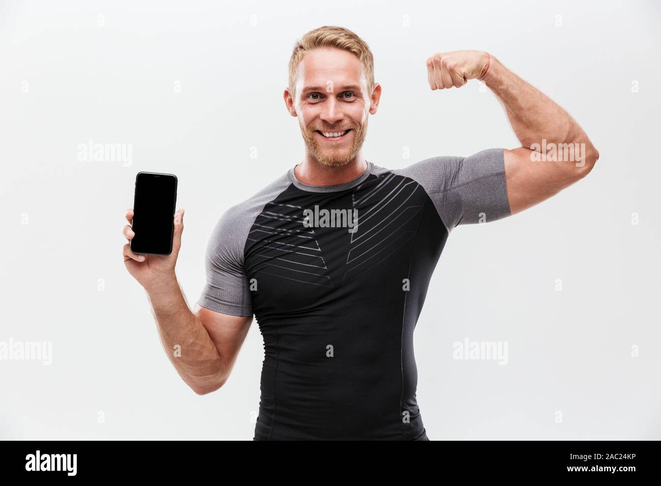Portrait of a smiling fit sportsman showing blank screen mobile phone ...