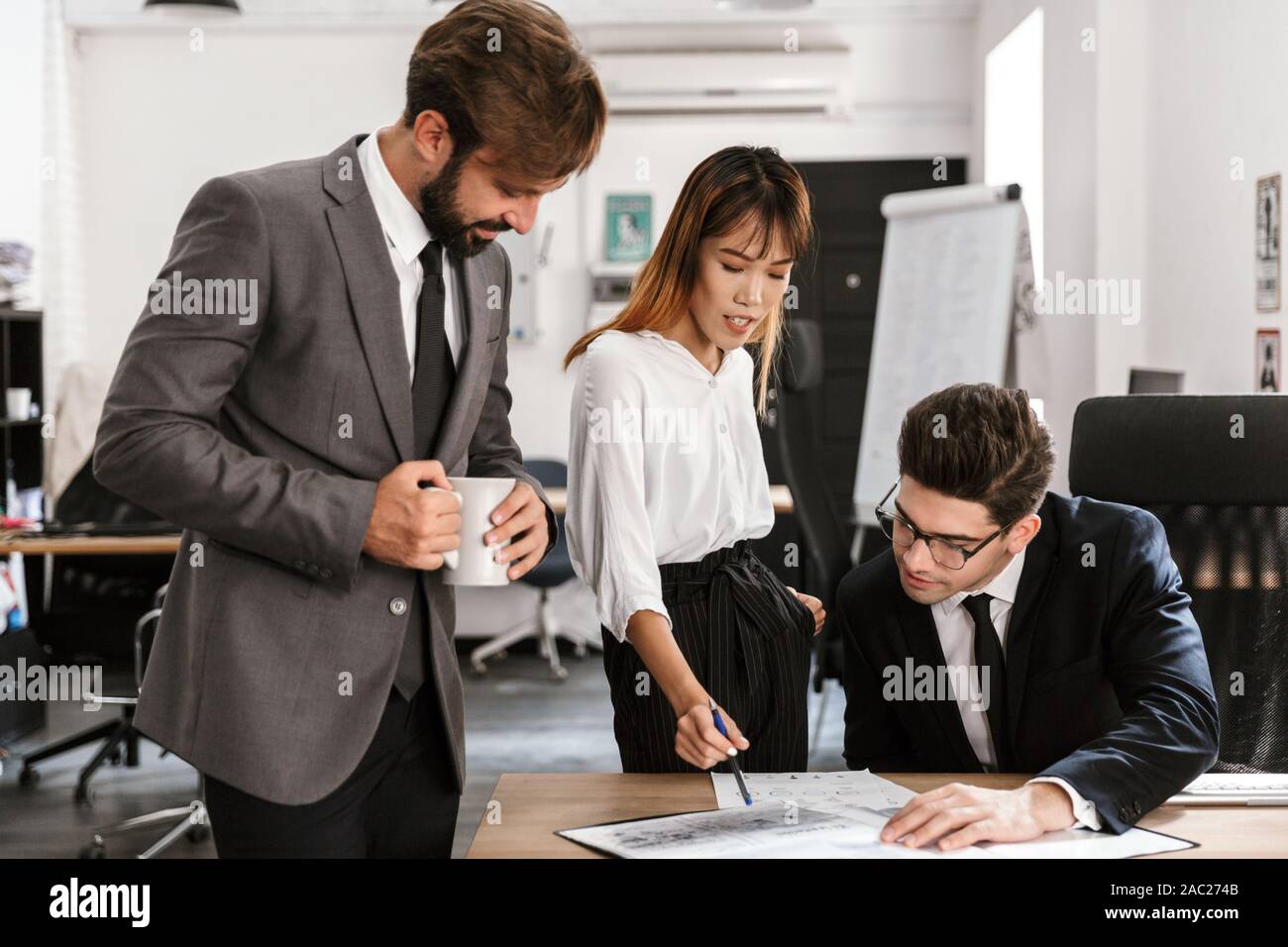 Photo of focused colleagues discussing project and drinking coffee while working in open-plan office Stock Photo