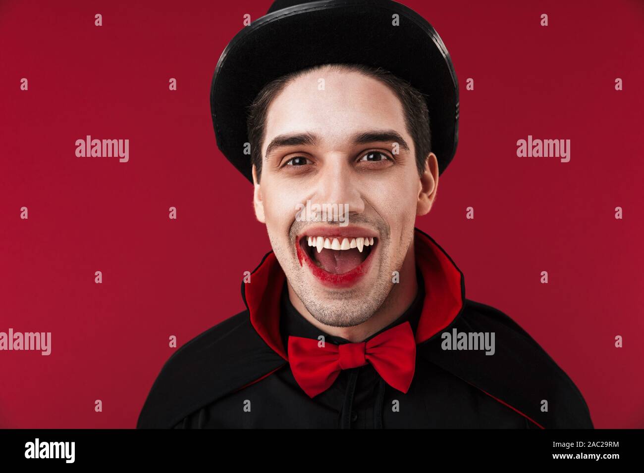 Image Of Young Vampire Man With Blood And Fangs In Black Halloween Costume Smiling Isolated Over Red Wall Stock Photo Alamy