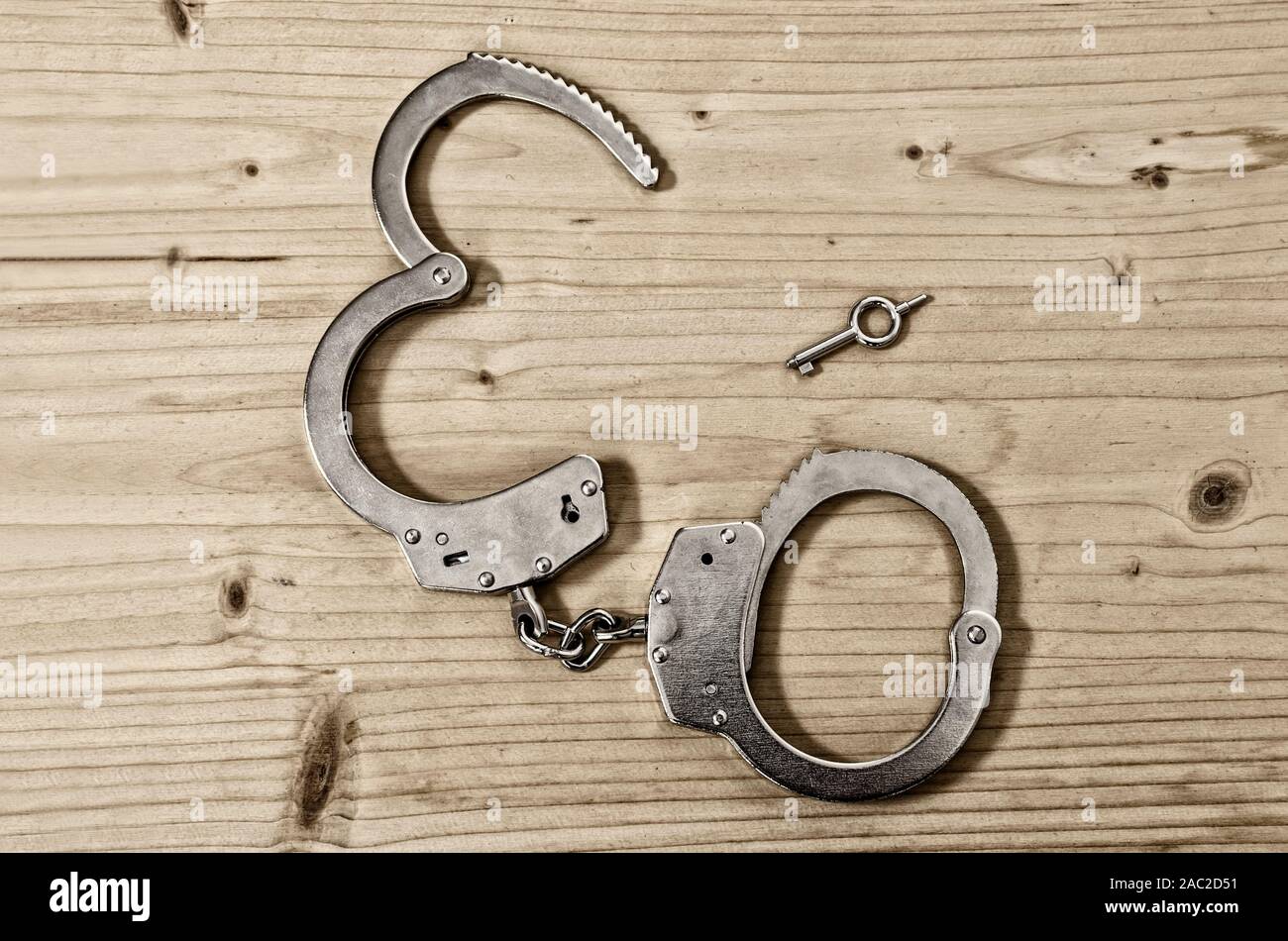 Top view of open handcuffs and key on a wooden table close-up. Crime and violence concept Stock Photo