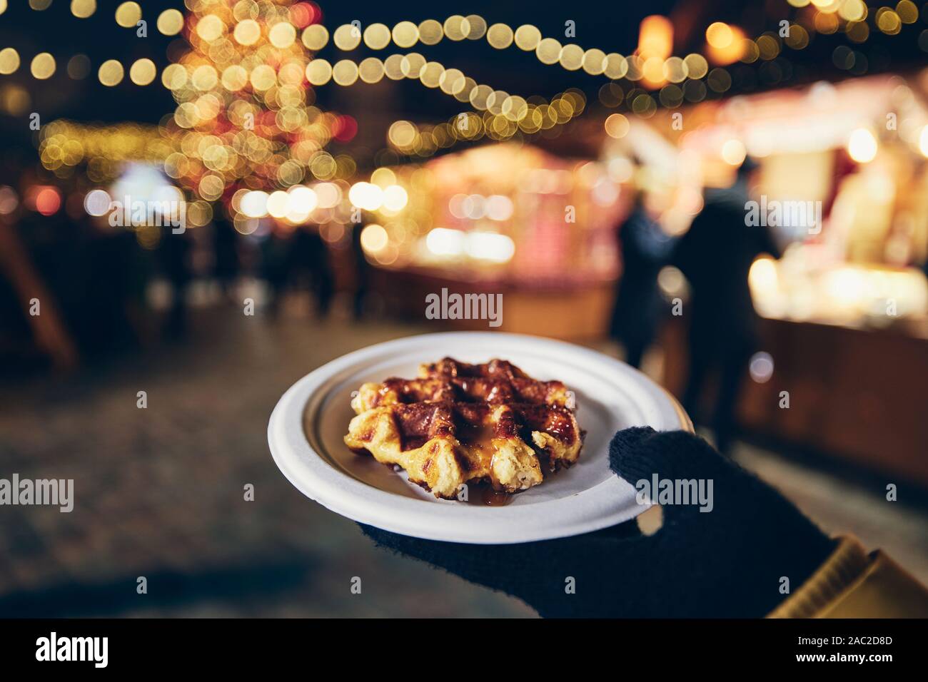 Hand in winter glove holding waffle with melted chocolate. Christmas market in Tallinn, Estonia. Stock Photo