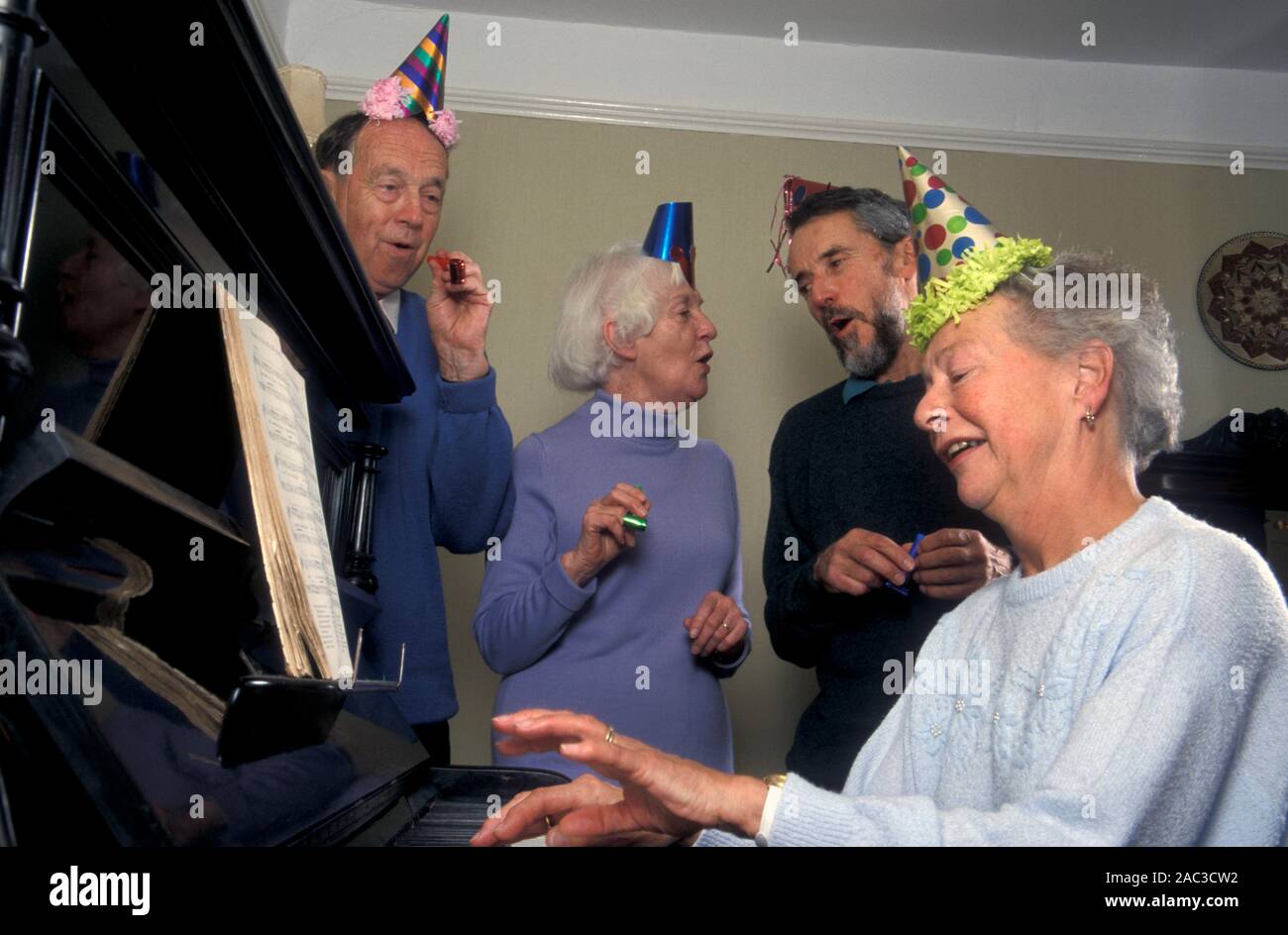 Senior couples in party hats having sing song around piano at Christmas Stock Photo