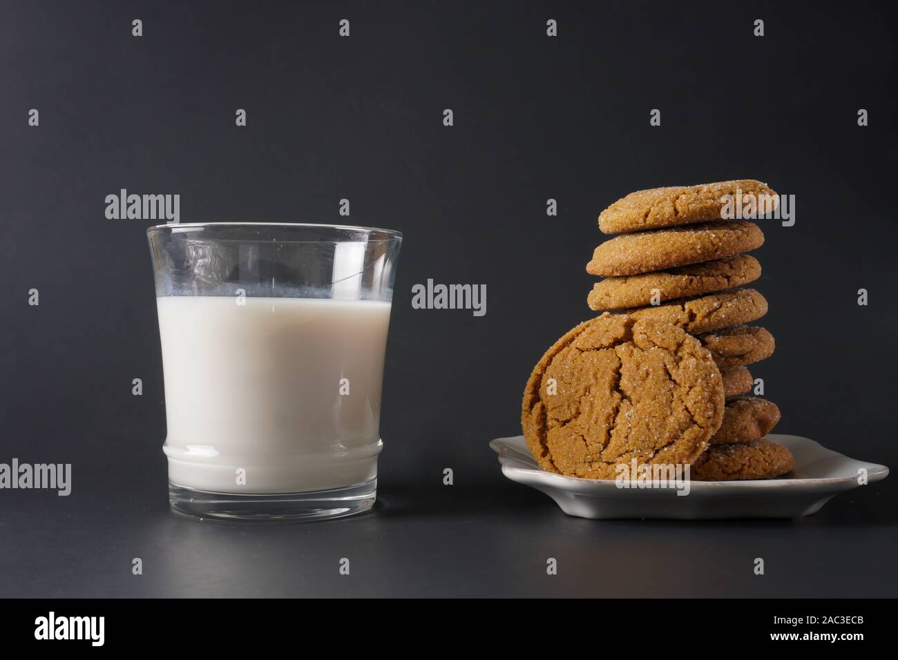 A glass of cold milk next to a stack of gingerbread cookies on a white plate with a black background; copy space Stock Photo