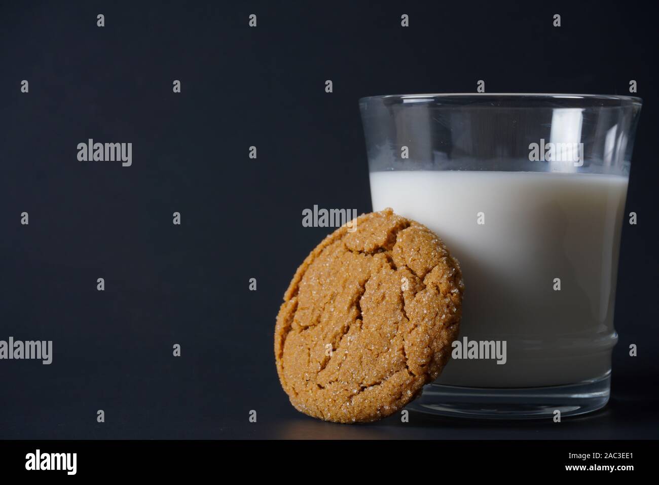 Close-up image of a gingerbread cookie leaning up against a cold glass of milk with copy space on the left Stock Photo