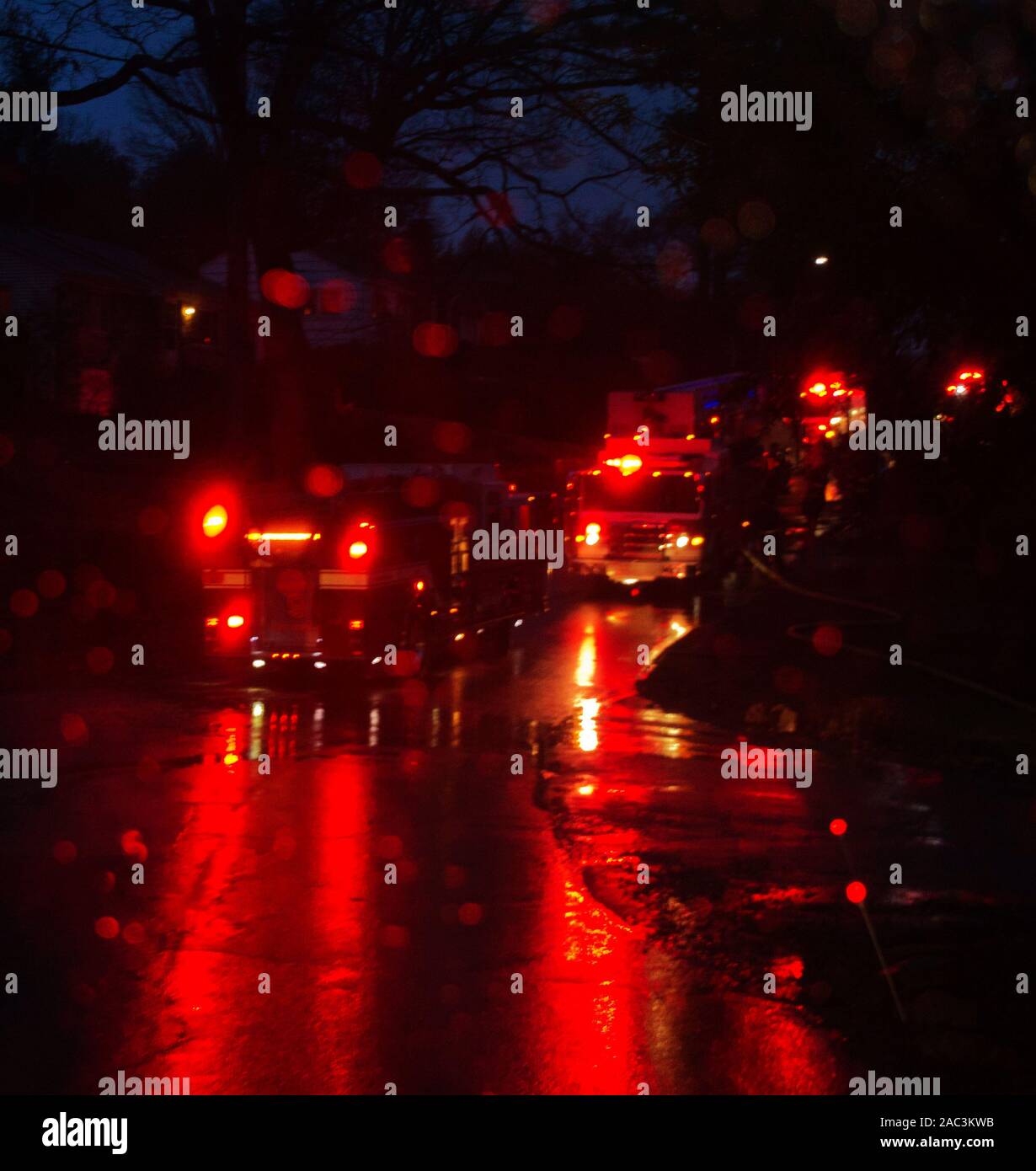 Emergency vehicles with red lights flashing line a wet road at night
