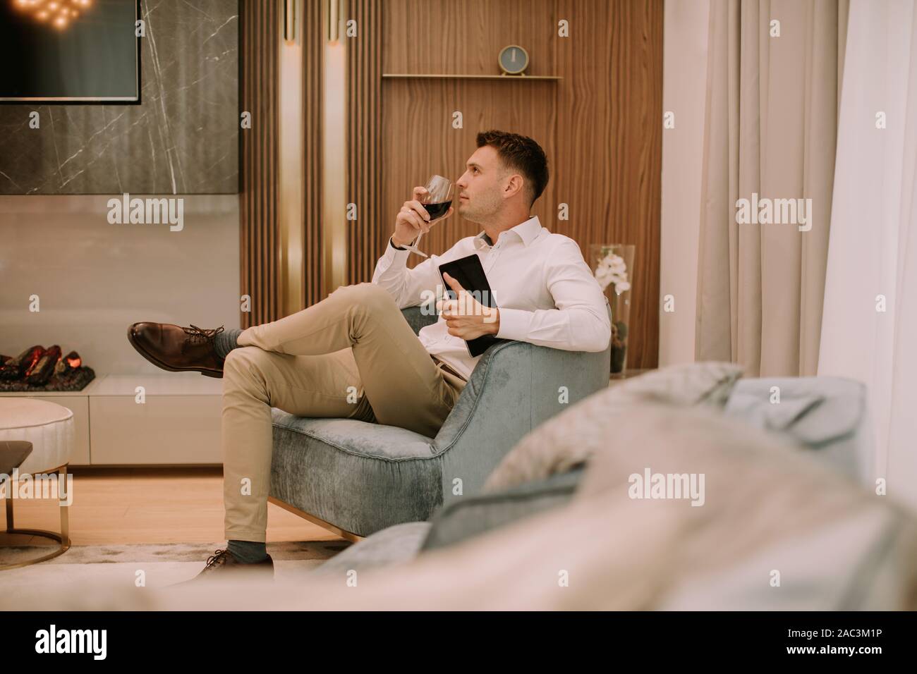 Young man sits in a luxury apartment, drinking red wine and holding a digital tablet Stock Photo