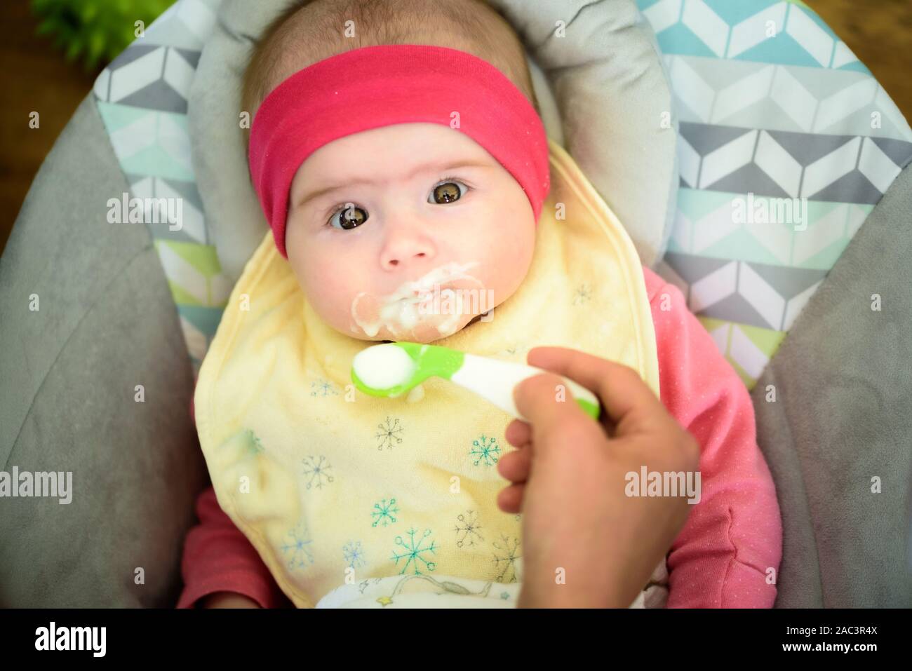 Mother feeding hungry five month old baby with spoon, solid food. Newborn feeding concept Stock