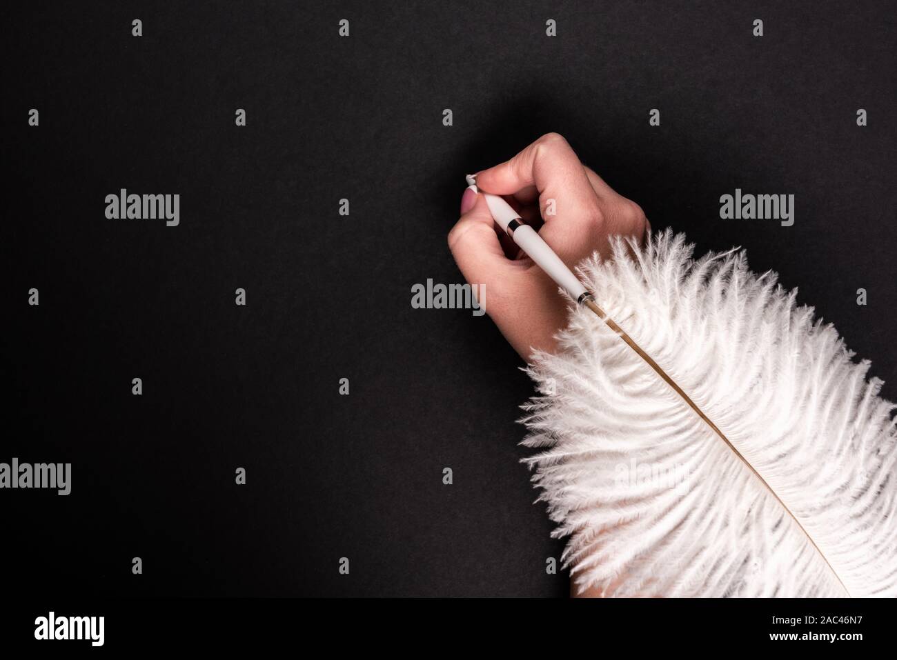 Female hand holding feather pen over black background Stock Photo