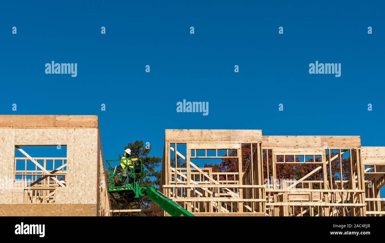 Construction worker elevated in hydraulic platform working on building with blue sky in background Stock Photo