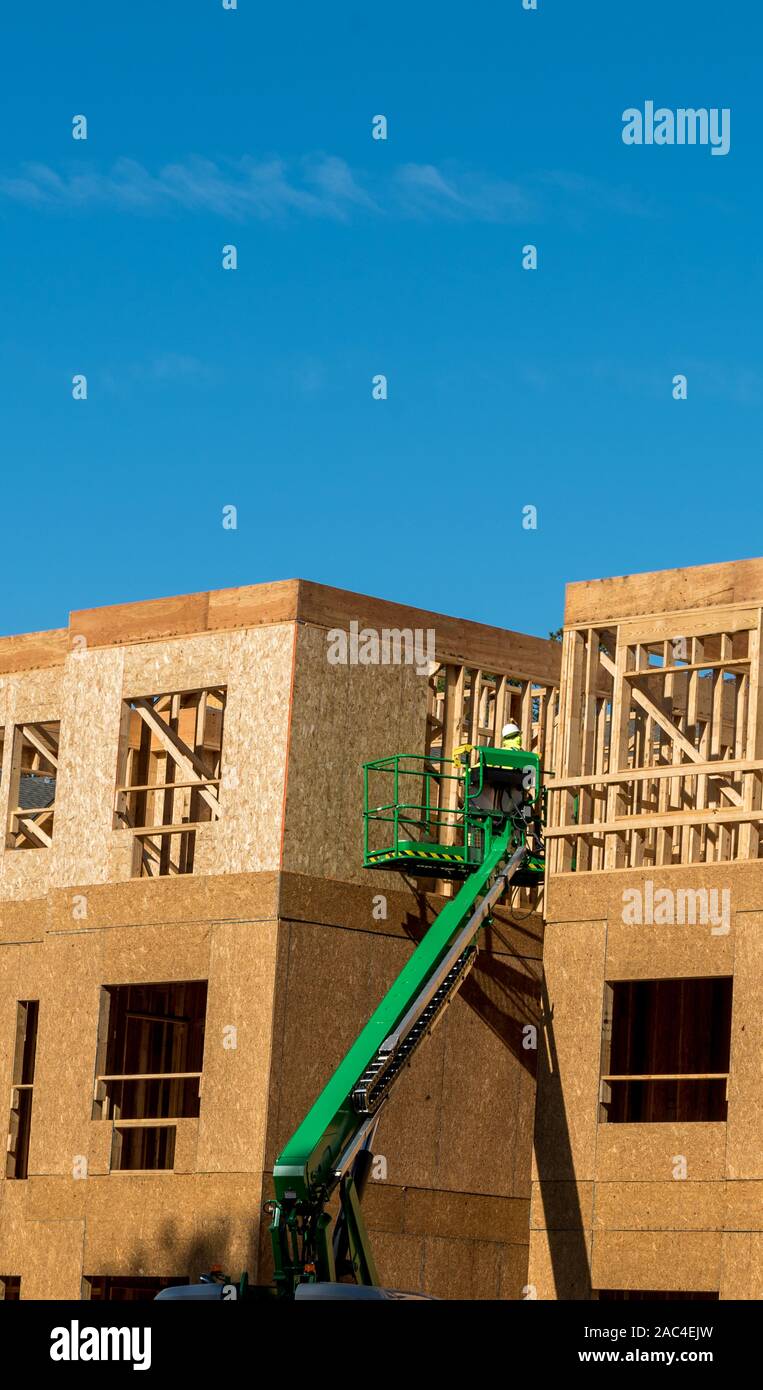 Construction worker elevated in hydraulic platform working on building with blue sky in background Stock Photo