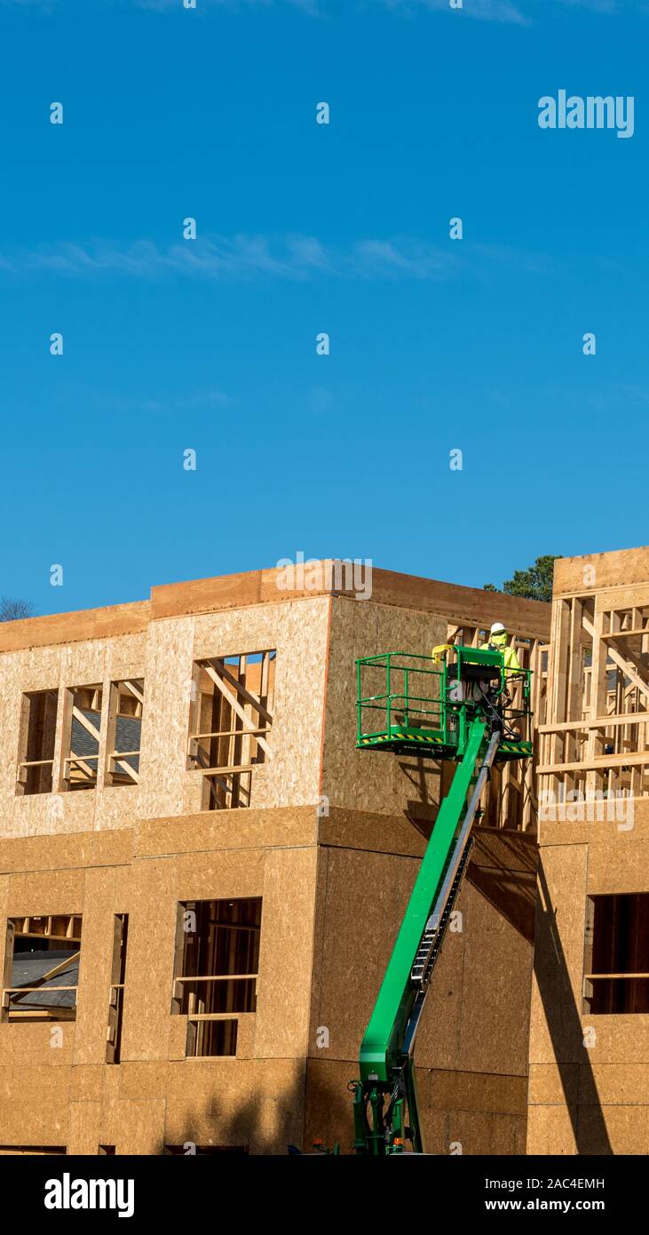 Construction worker elevated in hydraulic platform working on building with blue sky in background Stock Photo