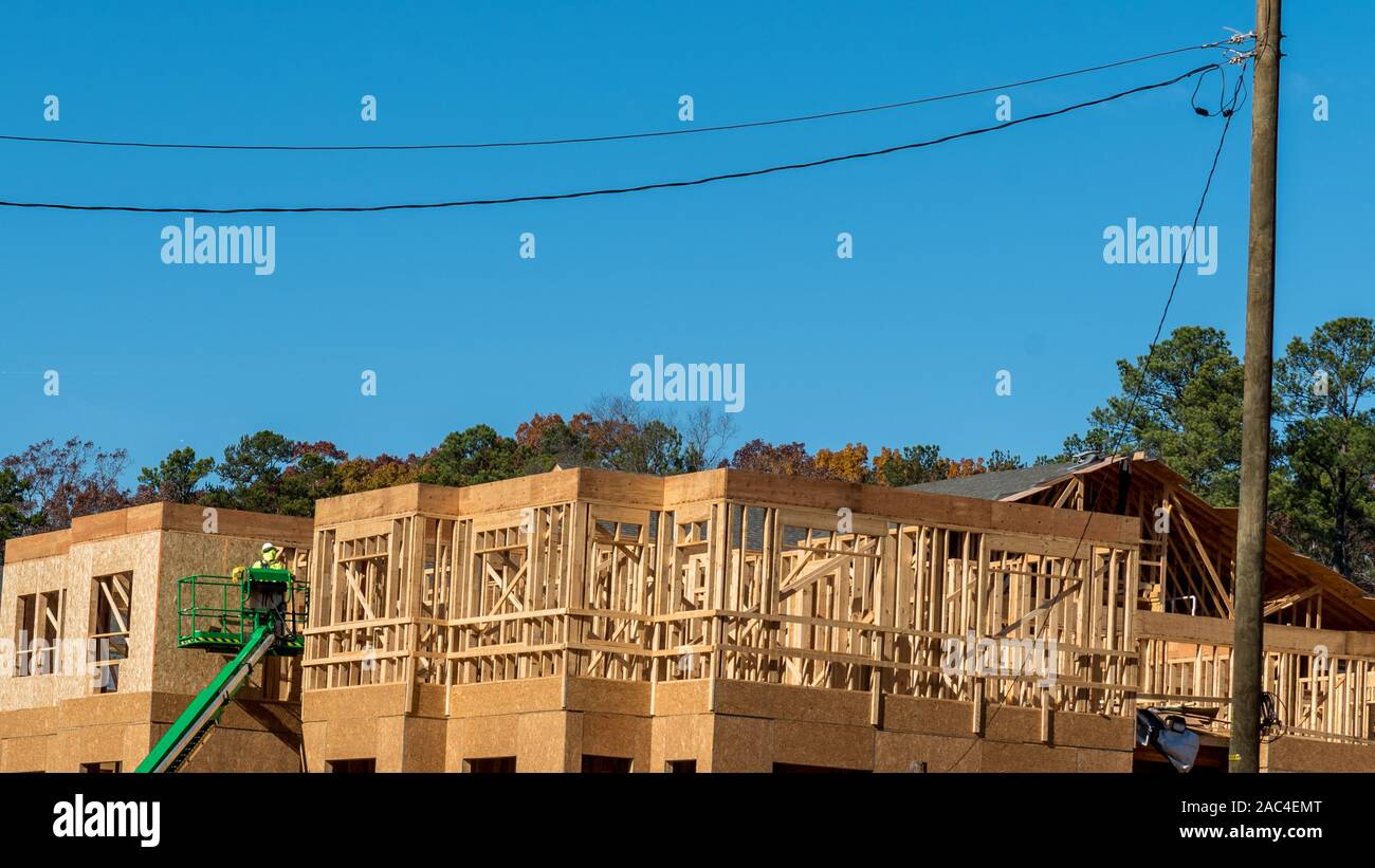 Construction worker elevated in hydraulic platform working on building with blue sky in background Stock Photo