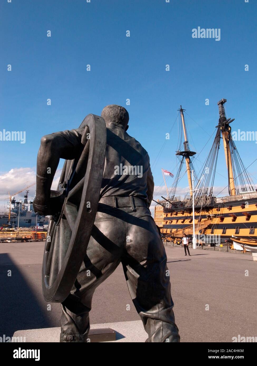 AJAXNETPHOTO. PORTSMOUTH, ENGLAND. - HISTORIC DOCKYARD BRONZE STATUE  - A FIELD GUNNER DEPICTED HEFTING A FIELD GUN WHEEL BY BRITISH SCULPTOR CHRISTOPHER KELLY. THE STATUE ON A PLINTH COMMEMORATES MEN FROM PORTSMOUTH COMMAND IN THE ANNUAL FIELD GUN COMPETITION AT THE ROYAL TOURNAMENT AND WHO TRAINED AT ROYAL NAVAL BARRACKS FROM 1947-1999 WHEN THE TOURNAMENT ENDED. TO THE LIMIT AND BEYOND. NELSON'S 1805 BATTLE OF TRAFALGAR FLAGSHIP HMS VICTORY IS SEEN BACKGROUND. PHOTO:JONATHAN EASTLAND/AJAX REF:GR110111 3169 Stock Photo