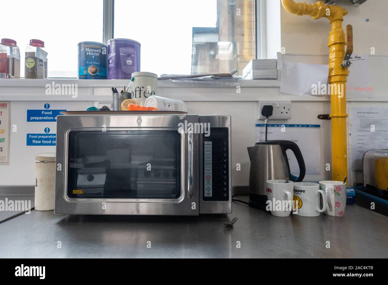 A microwave, electric kettle and mugs sit on a stainless steel worktop in a school kitchen. Stock Photo