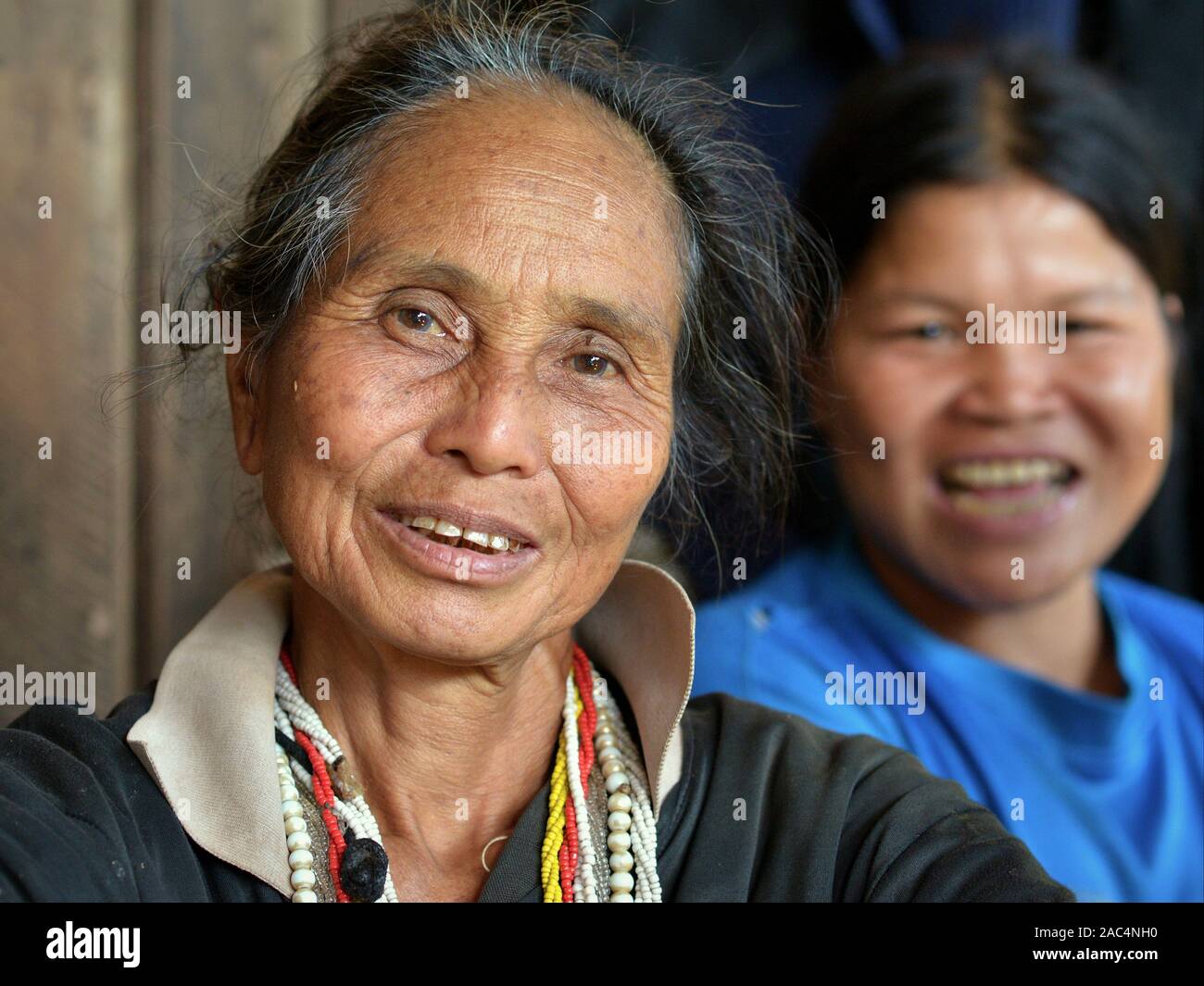 Elderly Thai Karen hill-tribe minority woman and young Thai Chinese woman smile together for the camera on the porch of their home. Stock Photo